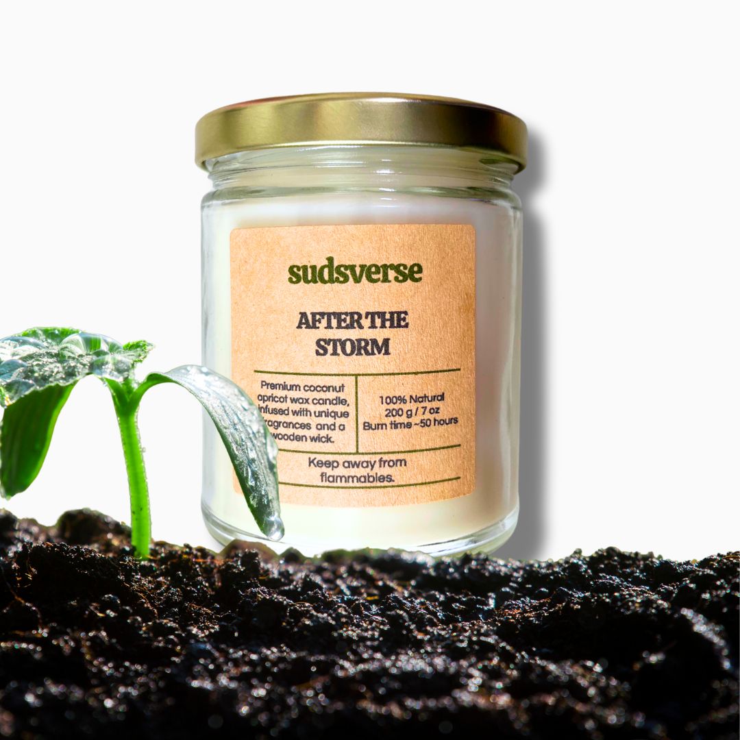 After The Storm Petrichor scented candle on a white background with wet soil and a plant depicting the scent of rain on the earth.