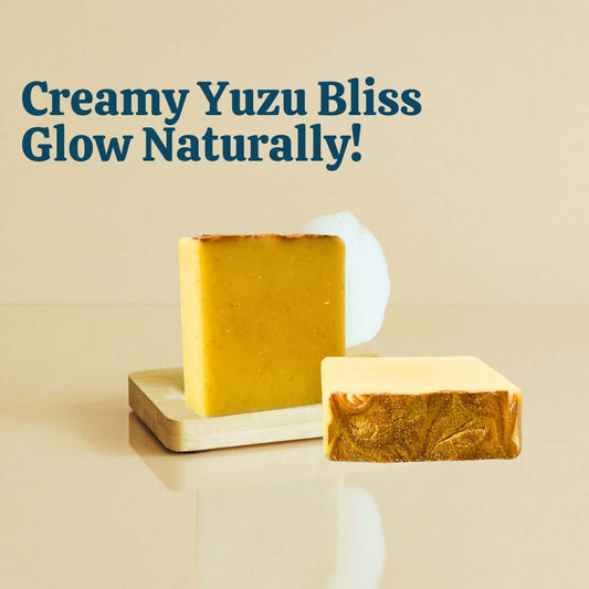 Sudsverse Creamy Yuzu Soap in dish with suds, yuzu, and vanilla on yellow marble. Text: Creamy Yuzu Bliss, Glow Naturally!