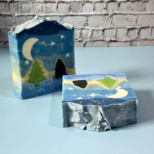 Two handcrafted Moonlit Grove natural soaps, one standing upright and one angled to showcase the detailed landscape design on the top of the bar